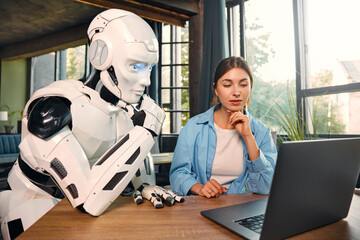 Robot and woman working on laptop in office
