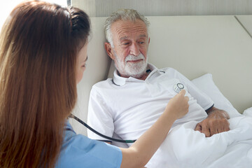 Elderly man feels sick and rest in bed at home with caring female nurse or doctor using stethoscope...