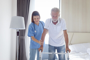 Female nurse or doctor helping elderly patient man lean to walk with orthopedic walker, patient practice walking inside house with physiotherapist, nursing senior people at house, medical health care.