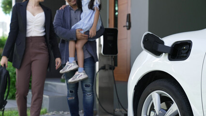 Fototapeta na wymiar Progressive young parents and daughter living in a home with an electric vehicle and electronic vehicle charging station. Green and clean energy from electric vehicles for healthy environment.