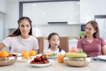 Happy family has meal in dining room. Parent mother, daughter and aunt sitting around dining table and having fun during breakfast. Cheerful family enjoy spending time together.