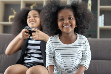 Joyful African sister girl with black curly hair enjoy play video game at home, two children hold...