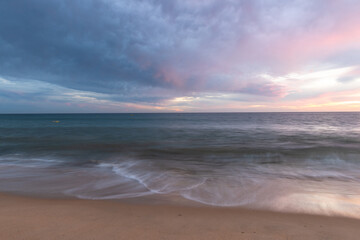 Fototapeta na wymiar Sunset on sandy beach with ocean waves and colorful sky and clouds, Algarve, Portugal