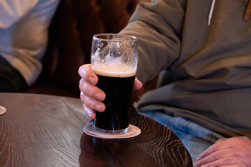 Man's hand holding a pint of beer in a pub