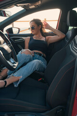 Fototapeta na wymiar Pretty woman with sunglasses is posing inside of a car at sunset