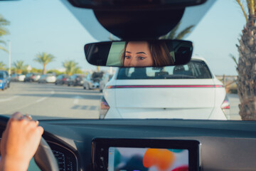 Naklejka premium Close-up of a woman driving in the interior of a car. Point of view of a driver to the street. Rearview mirror