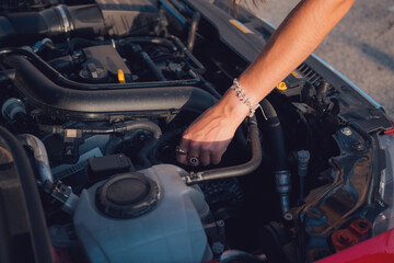 Close-up of a young woman looking at the engine of a car at sunset