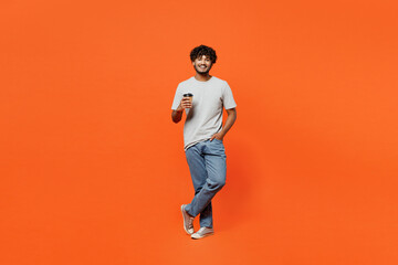Fototapeta na wymiar Full body young smiling happy Indian man he wearing t-shirt casual clothes hold takeaway delivery craft paper brown cup coffee to go isolated on orange red color background studio. Lifestyle concept.