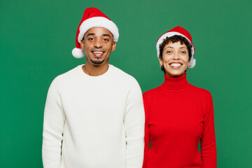 Merry smiling cheerful cool fun young couple friends man woman wear red casual clothes Santa hat posing look camera isolated on plain green background. Happy New Year 2024 Christmas holiday concept.