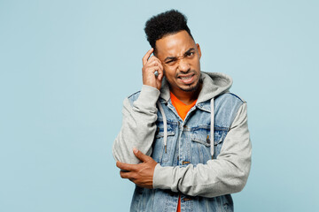 Young confused mistaken sad man of African American ethnicity wearing denim jacket orange t-shirt look camera scratch hold head isolated on plain pastel light blue cyan background. Lifestyle concept.