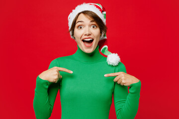 Young surprised shocked woman wear warm cozy green turtleneck Santa hat posing point index finger...