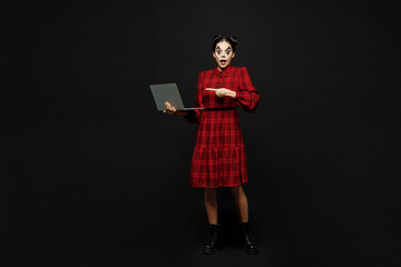 Full body young IT woman with Halloween makeup face art mask wear clown costume red dress hold use work point laptop pc computer isolated on plain black background studio. Scary holiday party concept.