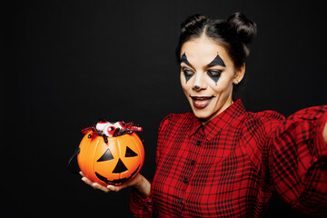 Young cool woman with Halloween makeup face art mask wears clown costume red dress do selfie shot mobile cell phone hold pumpkin isolated on plain black background studio. Scary holiday party concept.