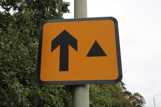 Orange road sign with arrow and black triangle to indicate a diversion route to direct traffic back onto motorway
