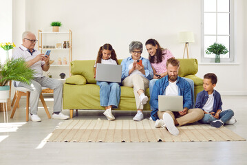Big family sitting in living room with gadgets, parents, grandparents and two children. Grandpa, mom and grandma looking at smartphones screens, daughter and father working on laptops with son.