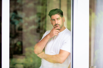 Close-up portrait of a man looking thoughtfully and standing behind windowpane