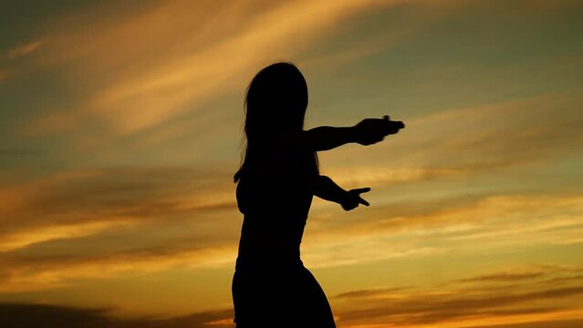 Woman with outstretched hands turning around dark silhouette outdoors