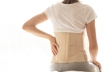 Woman with a corset on her back to support her back from pain in the back and spine, Medical concept, spinal support, wearing a brace at home