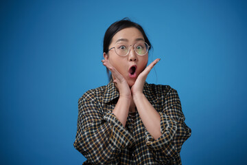 Asian woman looking on camera exciting and surprised, blue background.
