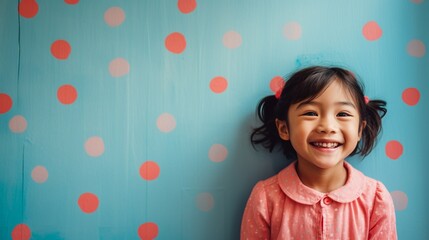 Happy cute Asian toddler girl wearing Polkadot colorful dress smiling and standing in front of blue and red painted wall, girl portrait with copy space. - obrazy, fototapety, plakaty