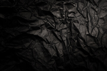 A sheet of black crumpled paper with folds and wrinkles. Dark paper texture