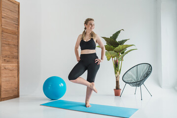 Plus size woman doing Pilates on a mat in a bright room. Yoga calm and balance