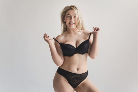 Plus size woman posing in black lingerie on a gray background. Attractive curvy blonde showing off her body with a smile