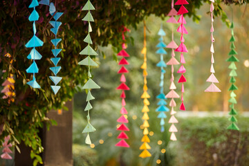 Fototapeta premium Outdoor decorations hanging from trees in green park, multicolored geometric tree decorations