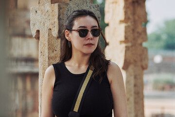 Attractive east asian woman in black sunglasses and black clothes stands among ancient pillars