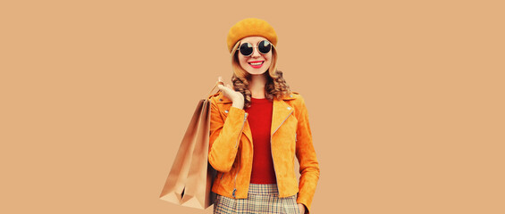 Autumn portrait of beautiful happy smiling young woman with shopping bags wearing orange french beret hat, jacket on brown studio background