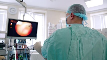 Rear view of male doctor standing near the patient. Surgeon is focused on the screen in front of him. Female nurse standing beside holding a tool prepared for surgeon.