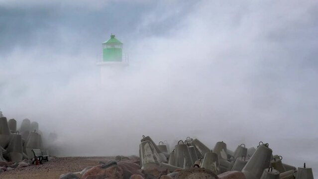 A 20 meter high wave crashes over the lighthouse at the end of the pier in slow motion during a storm