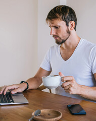 Serious male using laptop at desk in flat