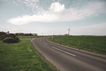 Road at the countryside of Kirkwall, Scotland with residential Building and modern wind turbine at...