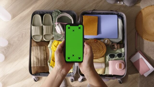 Hands phone green screen packed suitcase. Moving to apartment house emigration from country viewing browsing online ads in search of suitable place of residence. Template with chroma key phone screen