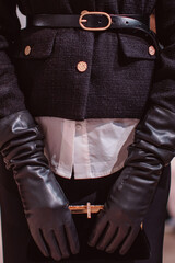 Fashion details of a classy black jacket, leather belt, gloves and classic velvet clutch. Fashion model posing on backstage