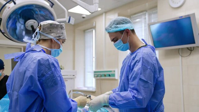 Male surgeon and assisting nurse prepare laparoscopic tool to use it in surgery. Minimal invasion operation on knee in modern hospital.
