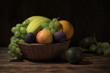 still life with fruit in a basket, bananas, grapes, nectirines, orange, figs and avocado