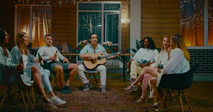 Friends spending summer evening in backyard, singing songs by guitar and drinking beer, 4K, Prores