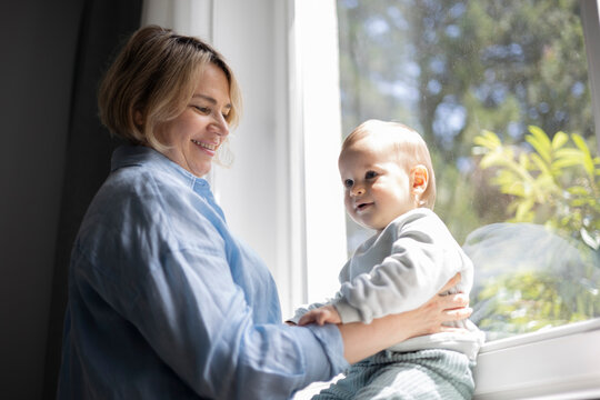 Mature blond woman and a baby boy near the window at home