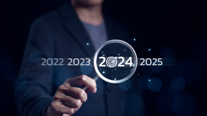 The 2024 year business goals concept. Businessman use magnifying glass search with 2024 wording for marketing monitor and business target planning for growth new year. Finding information, New ideas,