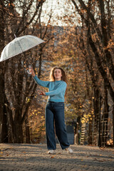 Young woman with transparent umbrella happy smiles. Student with curly hair poses in autumn park
