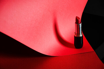 Red lipstick is lying on the top of a red paper background