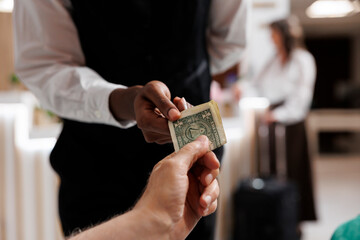 Close-up shot of retired senior male traveler providing cash tip to african american bellboy for helping in hotel reception. Caucasian elderly man thanking waiter great service, money for assistance.