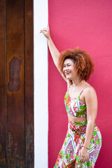 Beautiful redhead woman in long colorful dress standing against a red wall.