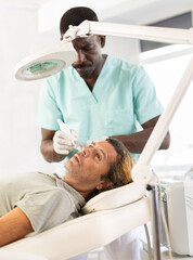 Male cosmetic doctor meticulously performs cosmetic procedure on another man, utilizing hydrogen...