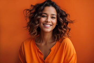 Portrait of a young beautiful smiling caucasian woman with curly hair wearing orange clothes on an orange background
