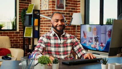 Upbeat smiling african american man enjoying his stay at home freelancing job, sitting at comfortable desk in stylish warm apartment. Cheerful happy teleworker working from home, close up