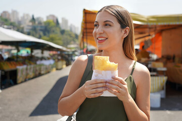 Close-up of beautiful girl eating Brazilian traditional food Pastel de Feira in Sao Paulo, Brazil