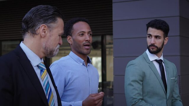 Side view three diverse serious business men communicating walking outdoors. Co-workers in suits discussing concerned strolling together outside office. Professional people and working relationships.